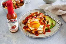 Load image into Gallery viewer, A plate with a fried egg drizzled with Mezzetta Roasted Red Pepper Hot Sauce
