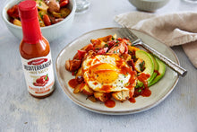Load image into Gallery viewer, A plate with a fried egg drizzled with Mezzetta Roasted Red Pepper Hot Sauce