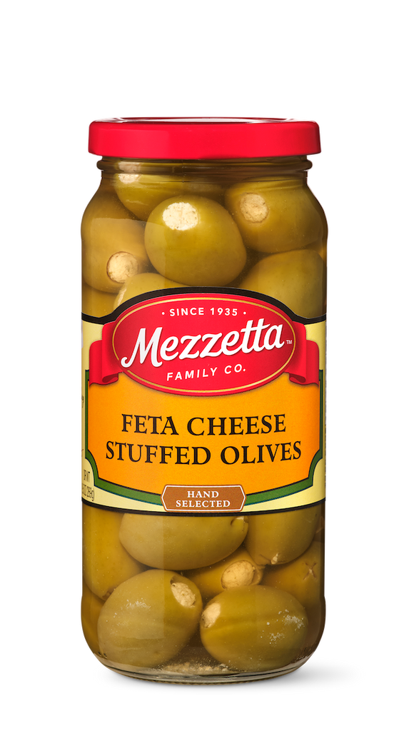 A glass jar brims with hand-selected green olives stuffed with feta cheese, showcasing the Mezzetta Family Co. brand.