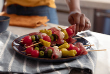 Load image into Gallery viewer, Plate of antipasto skewers with a hand grabbing one
