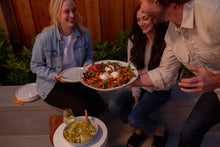 Load image into Gallery viewer, Man serving two women a plate with burrata and tomatoes
