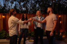 Load image into Gallery viewer, Four friends raise their glasses in a cheers gesture, enjoying drinks and conversation at an outdoor evening gathering.