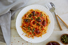 Load image into Gallery viewer, A plate of Pasta Puttanesca made with Kalamata olives and capers and utensils
