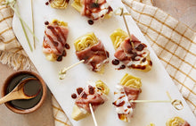 Load image into Gallery viewer, A platter of Prosciutto Wrapped Artichoke Hearts drizzled with balsamic.
