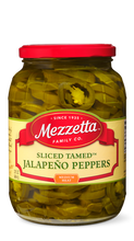 Load image into Gallery viewer, A clear glass jar filled with Mezzetta sliced tamed jalapeno peppers. The jar features a red lid and a label describing the product's medium heat level.