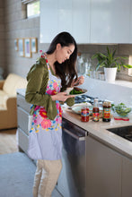 Load image into Gallery viewer, Woman adding sauce to her plate of food next to jars of Mezzetta Roasted Red Pepper, hot sauce, and Kona Coast Island Teriyaki
