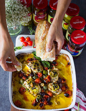 Load image into Gallery viewer, Hands dipping bread into a casserole dish of Mezzetta products and cheese