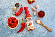 Load image into Gallery viewer, Roasted Red Pepper Hot Sauce jar next to peppers and garlic
