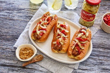 Load image into Gallery viewer, A plate with three grilled sausages in buns topped with Mezzetta Spicy Pickled Onions  

