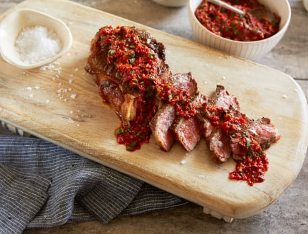 Seared Steak with Red Pepper Chimichurri Sauce served with salt on a wooden platter