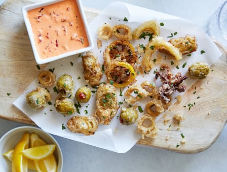 Frito Misto served with Roasted Red Pepper Aioli and lemons on a wooden board