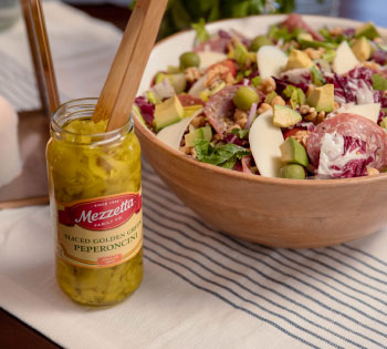 Jar of Mezzetta Sliced Golden Greek Peperoncini next to large salad