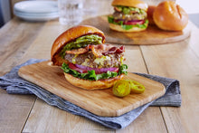 Load image into Gallery viewer, A cheesy pepper burger on a wooden board with two Mezzetta Sliced Jalapeno Peppers
