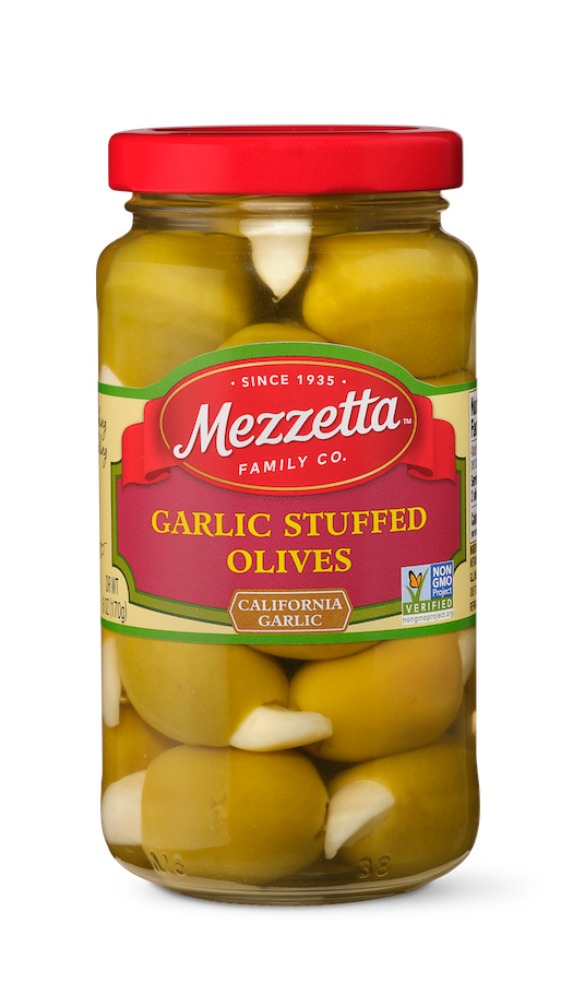 A glass jar filled with Mezzetta Garlic Stuffed Olives, each olive bursting with a plump garlic clove. 
