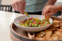 Load image into Gallery viewer, Two people dipping pita chips into a bowl of guacamole. 
