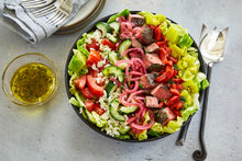 Load image into Gallery viewer, Large black bowl with Steak Chopped Salad and a small bowl of dressing
