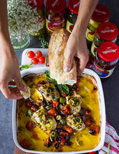Load image into Gallery viewer, Hands dipping bread into a casserole dish of Mezzetta products and cheese
